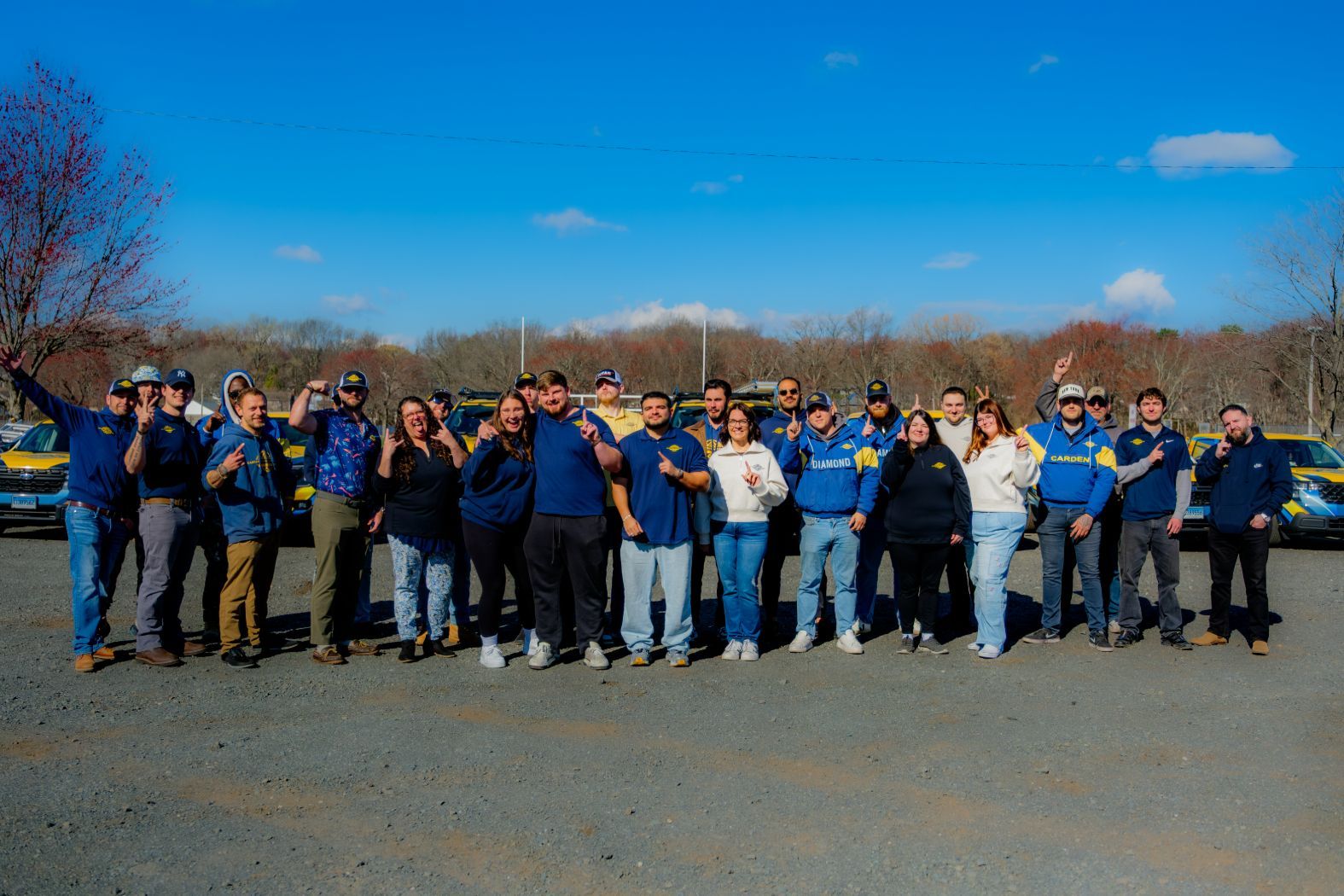 Group of people standing outdoors on a sunny day, posing together on a road with trees in the background
