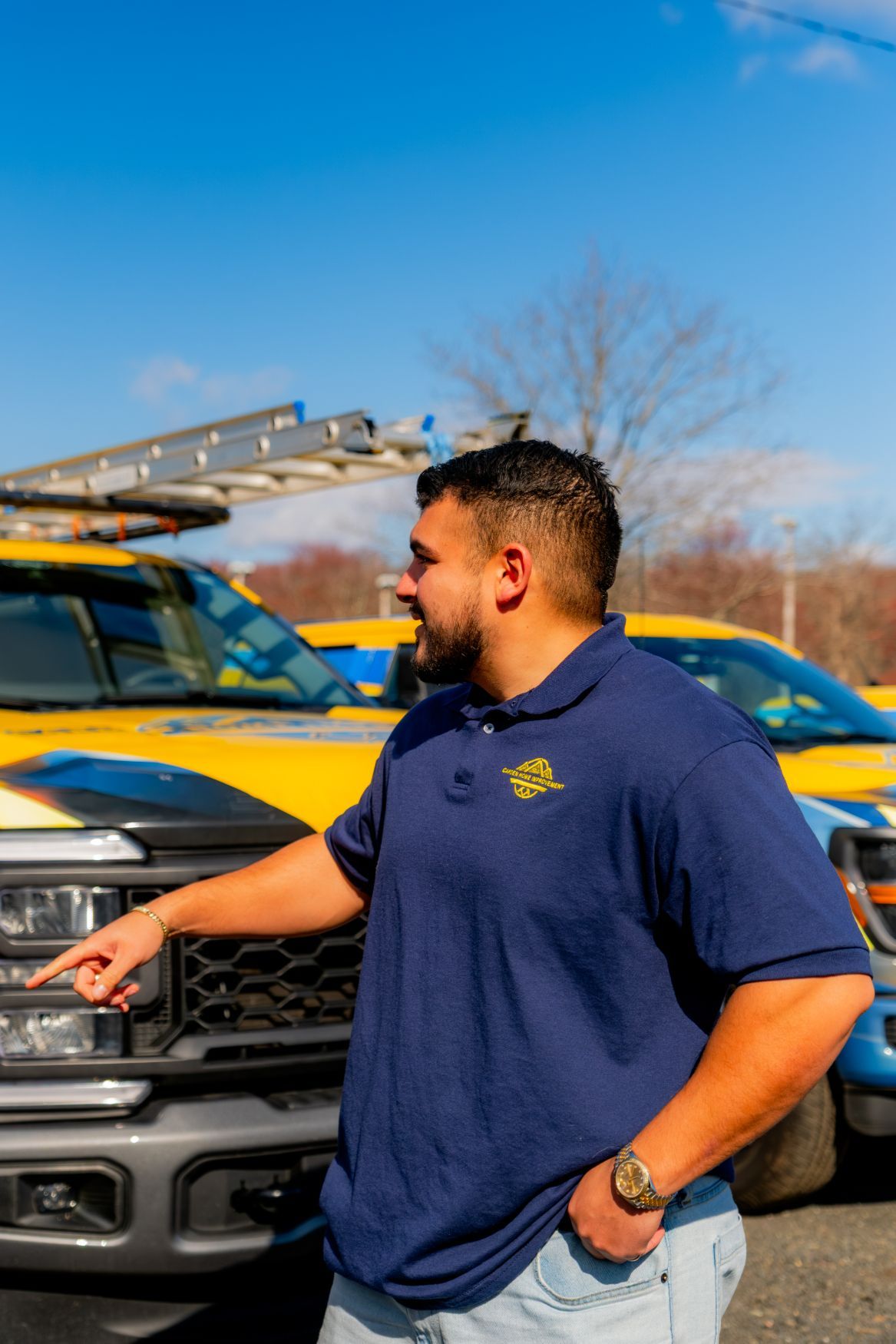 Man standing by yellow trucks, pointing and smiling outdoors under a blue sky