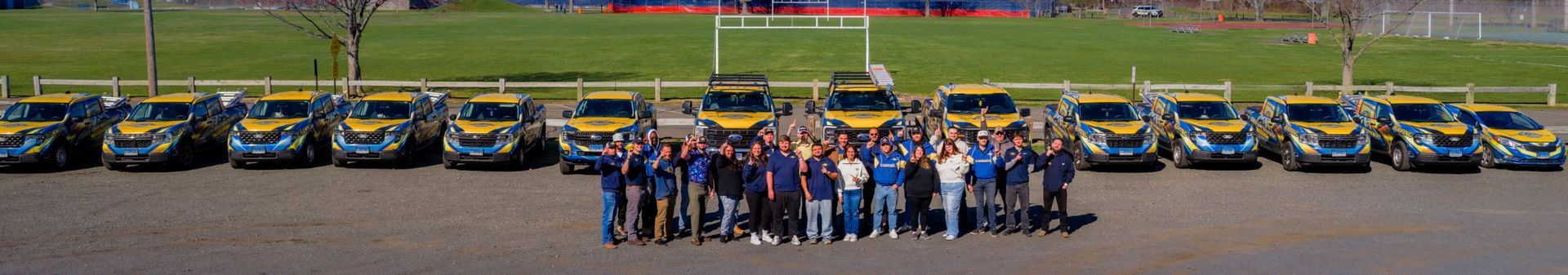 Group posing in front of a line of yellow race cars on a track