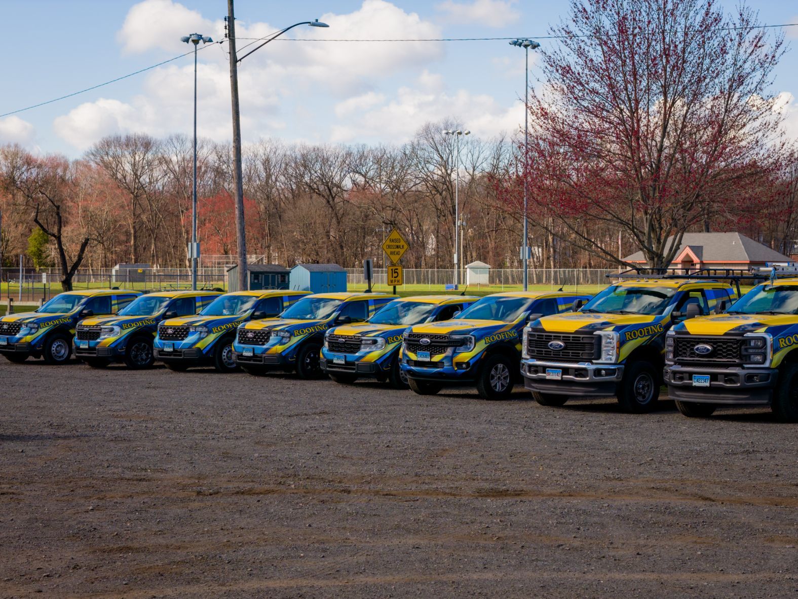 Row of blue-and-yellow utility trucks parked in an open lot on a cloudy day
