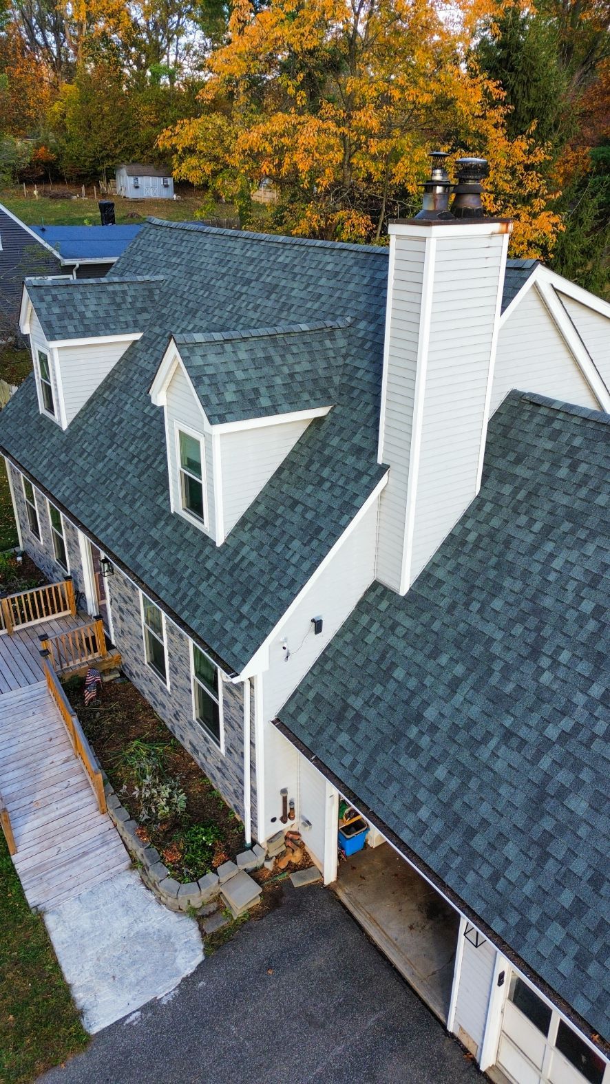 Aerial view of a white house with a gray shingle roof and brick chimney, surrounded by autumn trees.