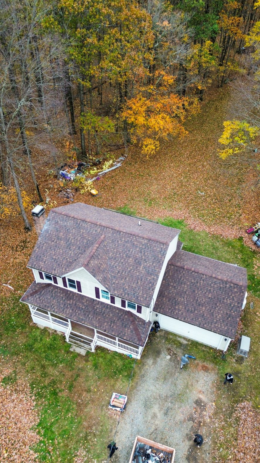 Aerial view of a house with a gray roof beside a driveway, surrounded by trees with autumn colors
