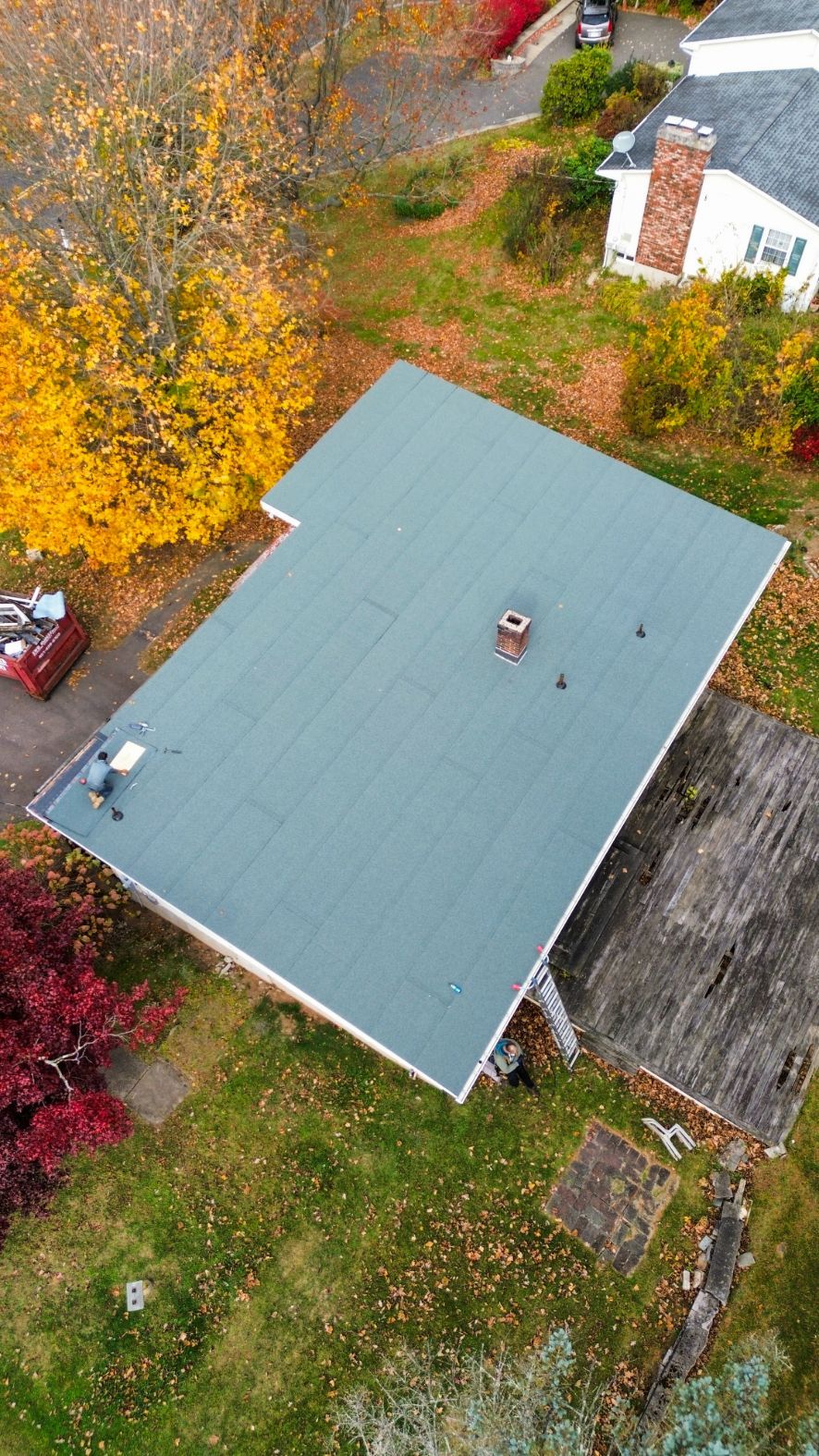 Aerial view of a house with a green roof surrounded by autumn trees and a grassy yard.