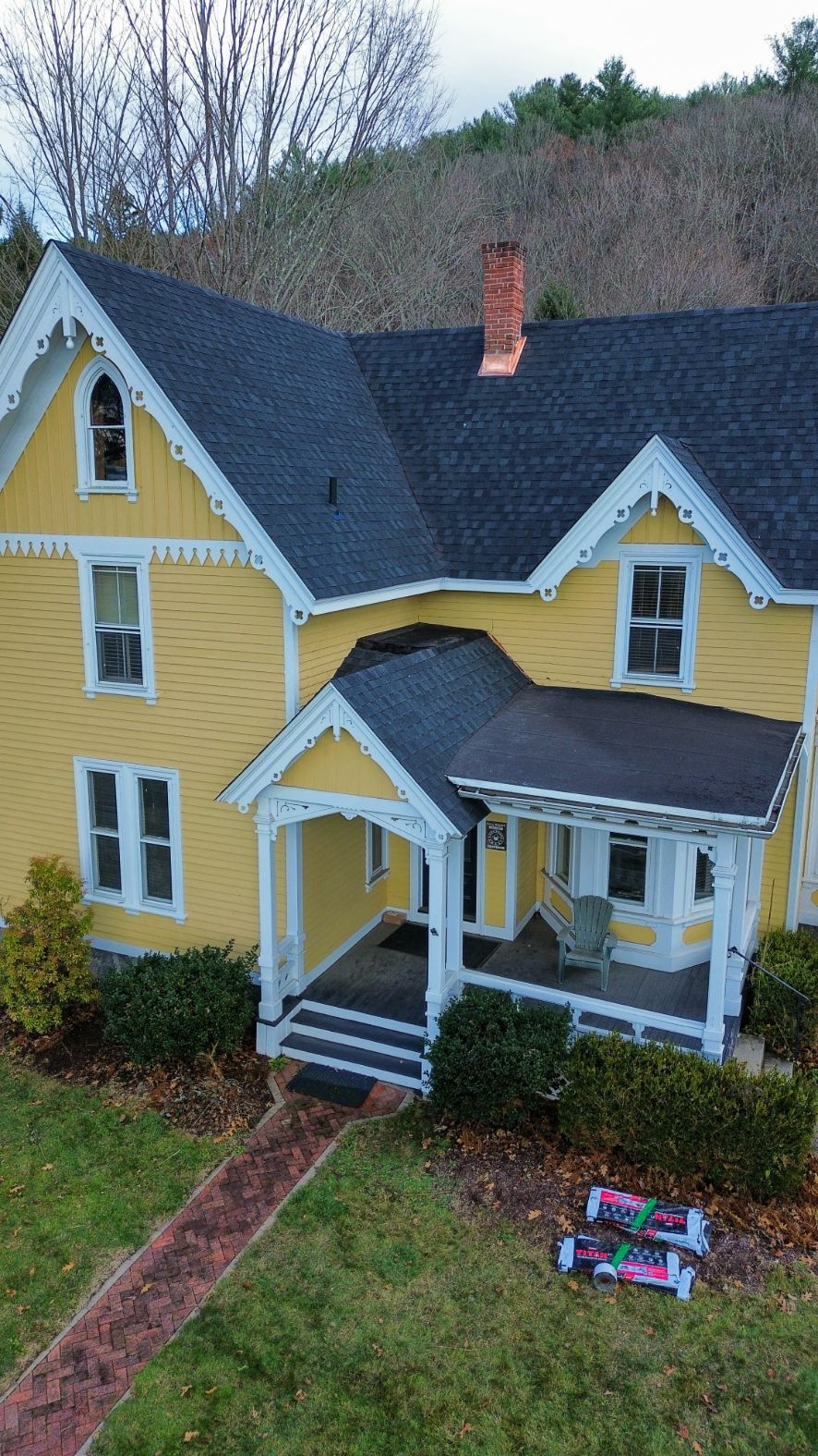 Yellow house with white trim, dark roof, and a small front porch beside a brick walkway.