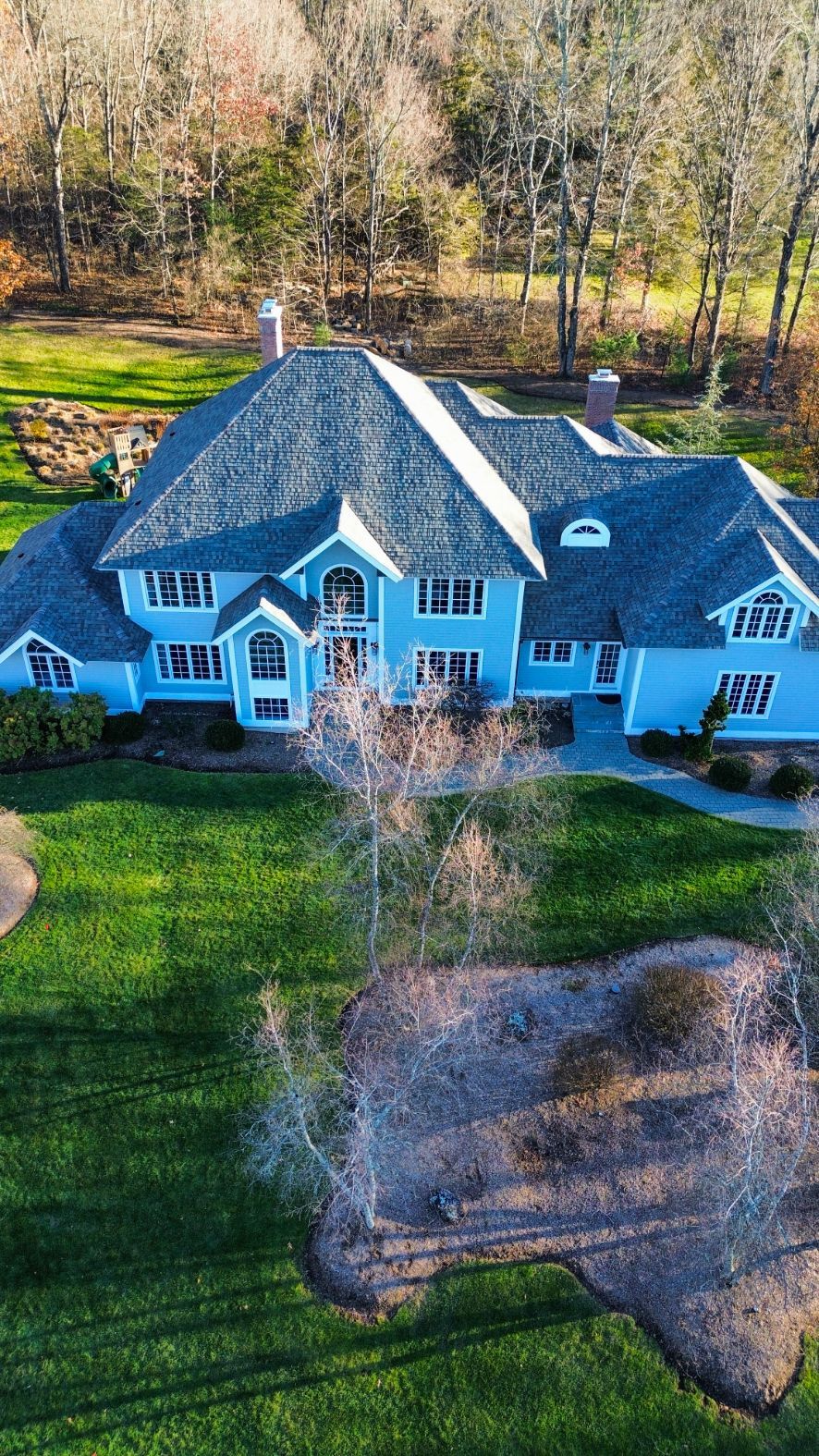 Aerial view of a blue house with a dark roof, front lawn, and trees in the background.
