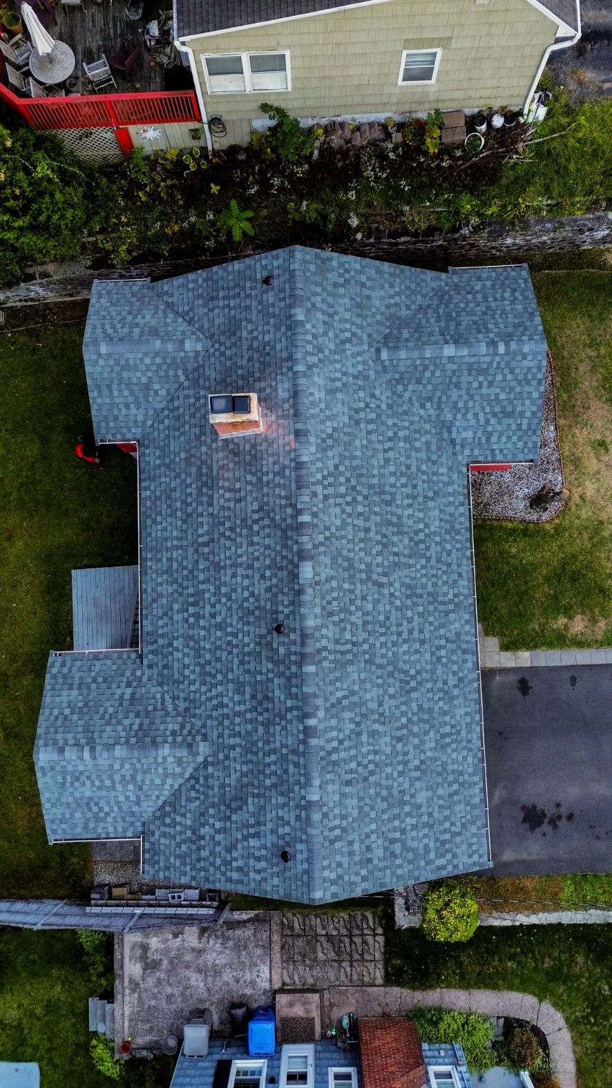 Aerial view of a blue-gray roof on a house with a small chimney and surrounding yard.