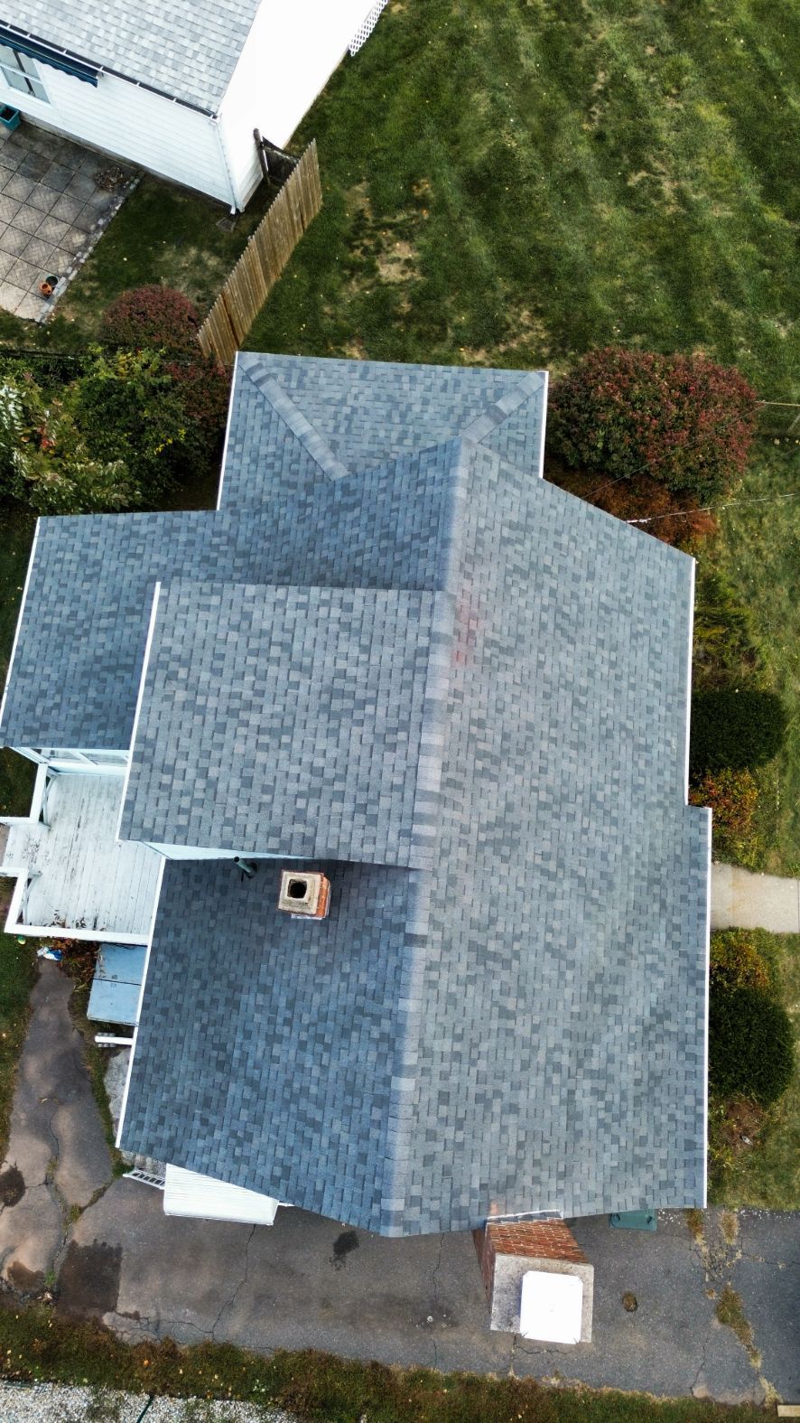 Aerial view of a gray-roofed house with a driveway and green yard surrounded by shrubs.