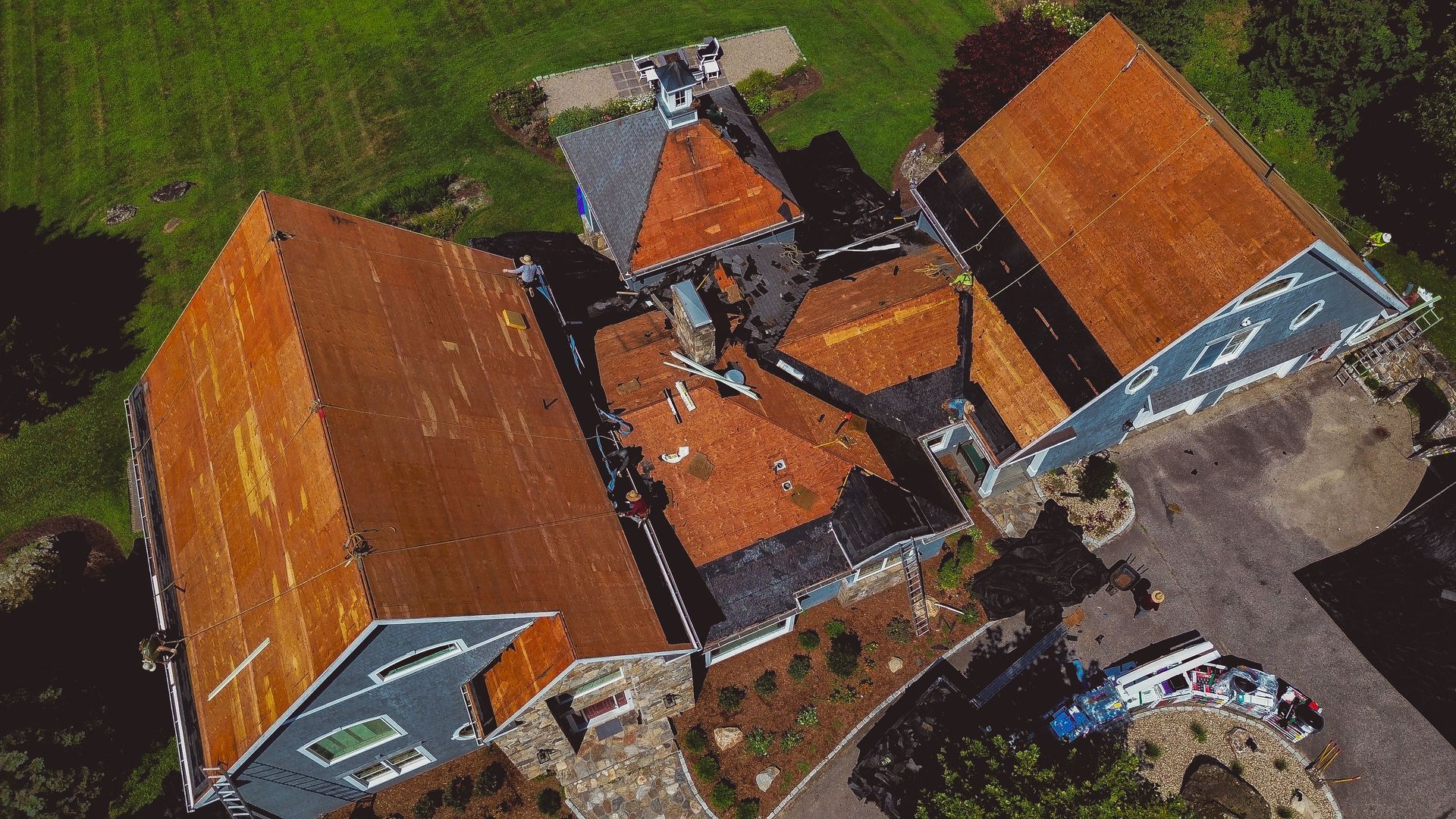 Overhead view of a house with orange and gray roofs and surrounding green grass and driveway.