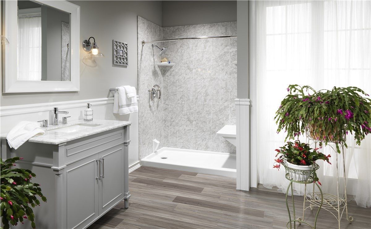 A modern bathroom featuring a gray vanity with a marble top, a glass-walled shower with tiled walls, and potted plants.