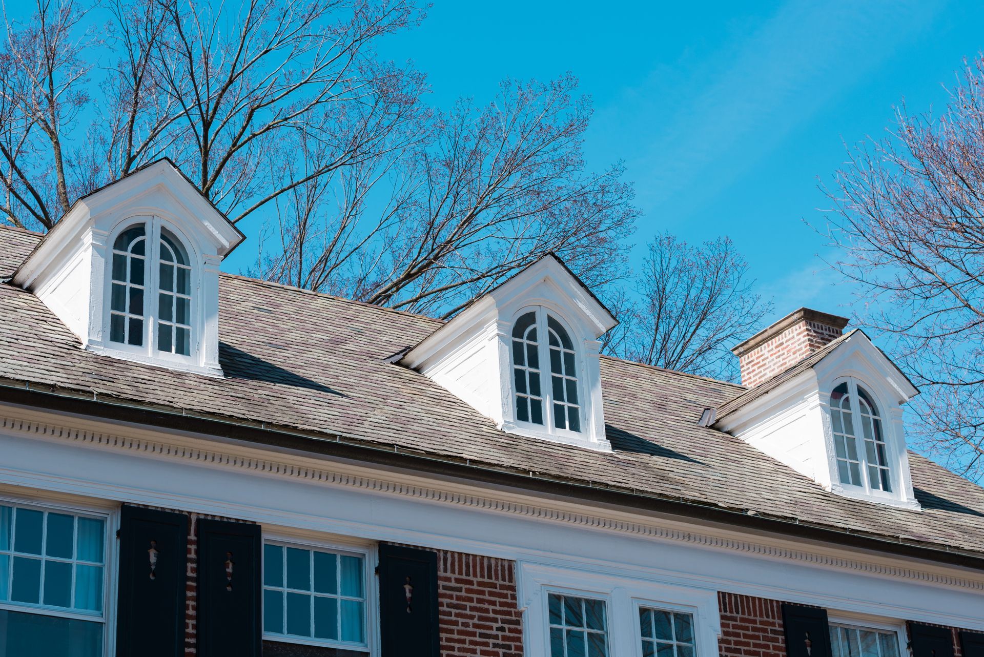 White dormer windows on a brick building under a bright blue sky