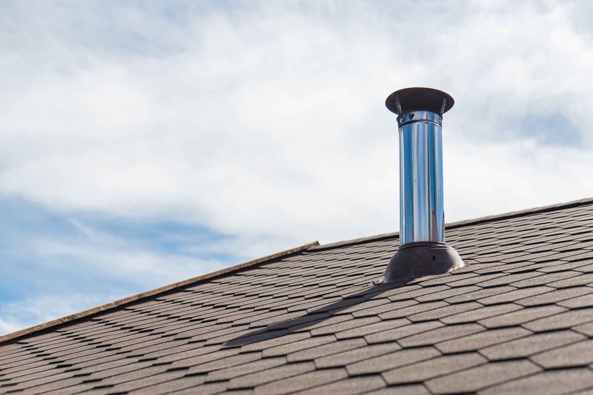 Shingled rooftop with a blue metal chimney against a cloudy sky