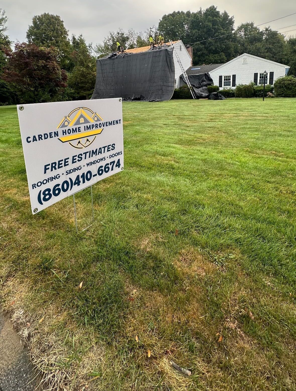 Lawn sign advertising free estimates for roof work in a grassy yard near houses