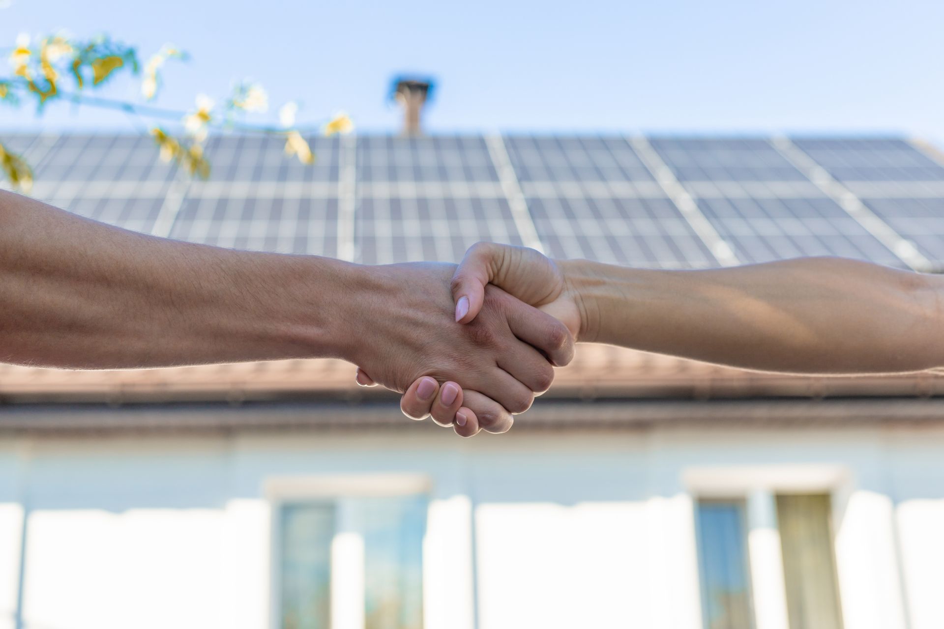 Two hands shaking in front of solar panels on a rooftop