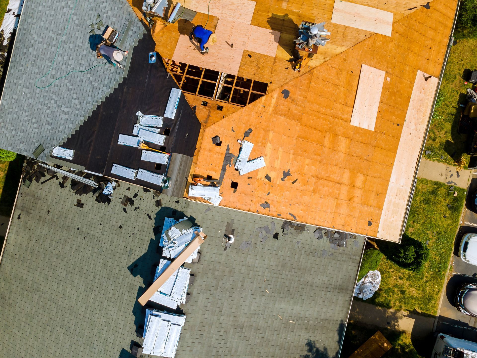 Aerial view of a rooftop under repair, with workers, tools, and orange and gray roofing sections