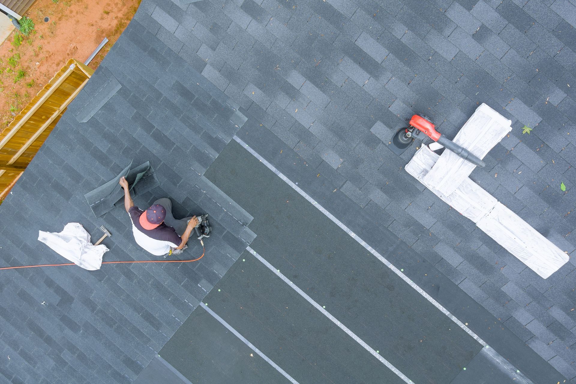Two roof workers installing white metal flashing on a gray shingle roof, aerial view