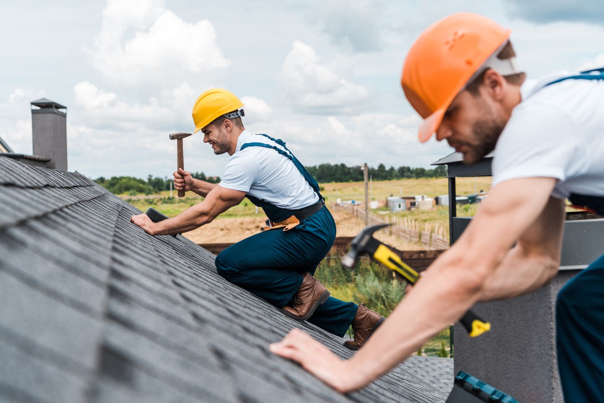 Two roofers in hard hats installing shingles on a roof under a cloudy sky