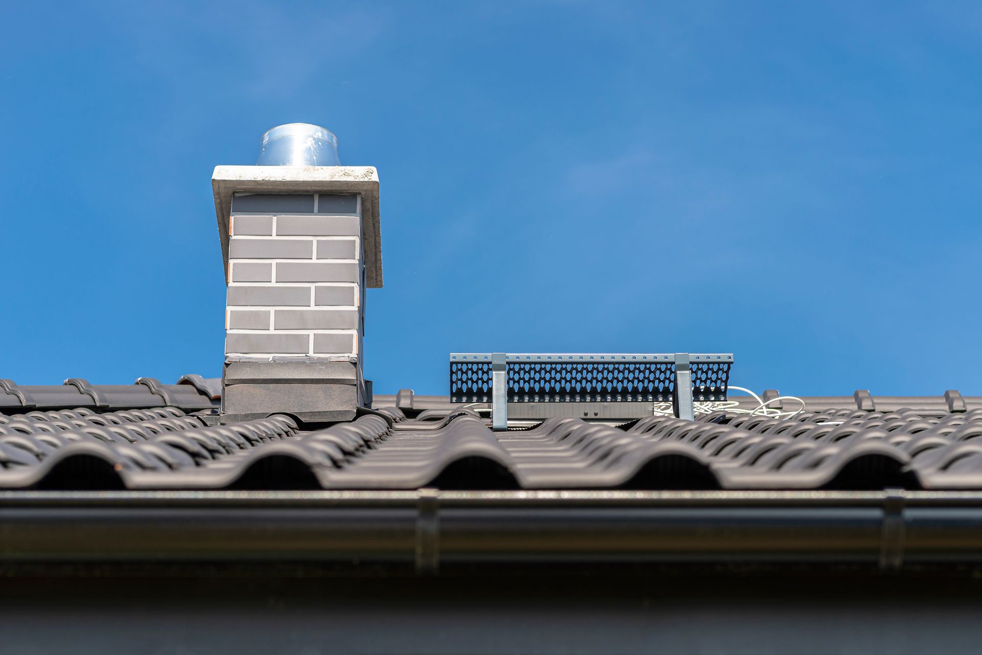 Rooftop with gray chimney and solar vent against a clear blue sky