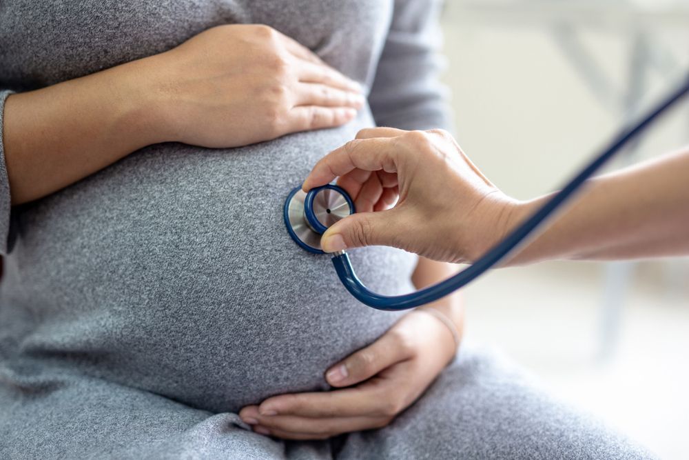A pregnant woman is being examined by a doctor with a stethoscope.