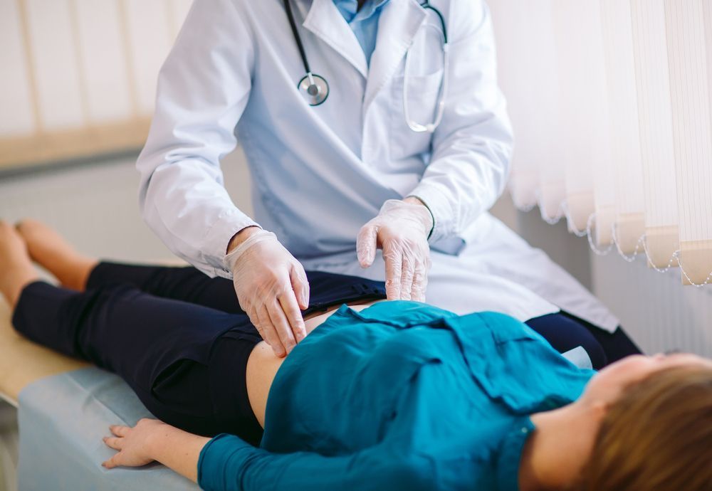 A woman is laying on a bed while a doctor examines her stomach.