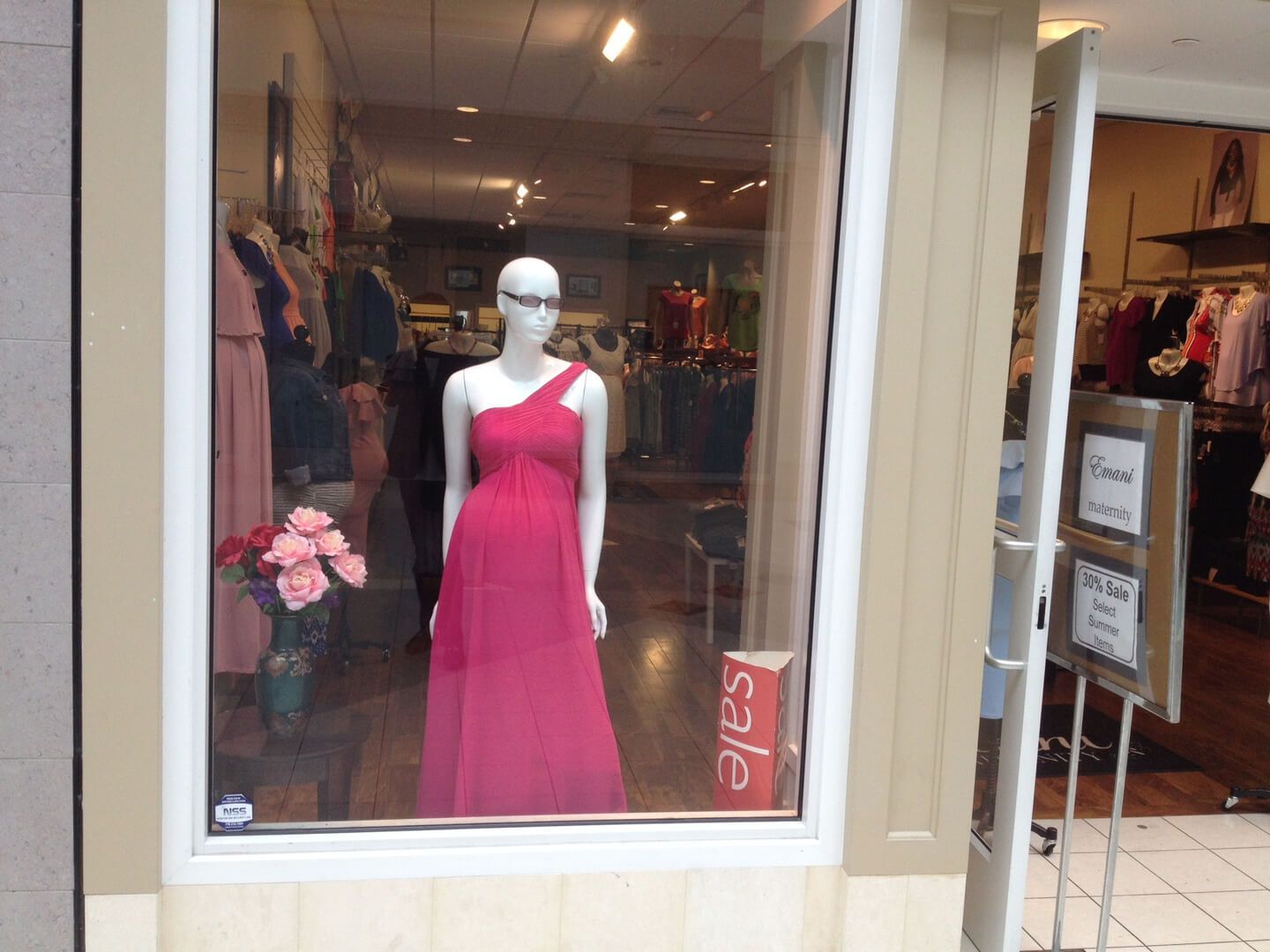 A mannequin in a red dress is in a store window with a sign that says sale