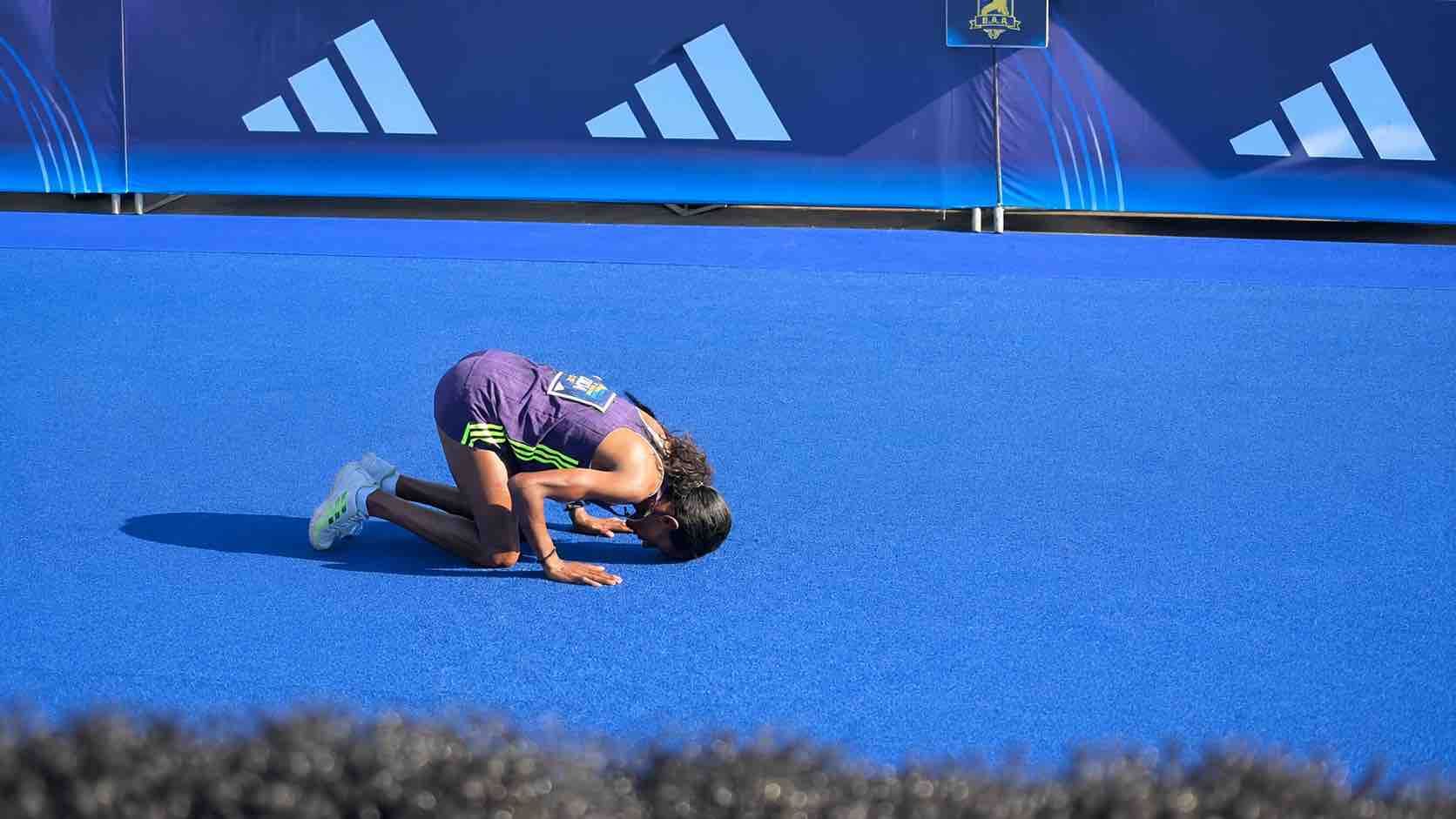 Sanlam Cape Town Marathon female winner kneeling on the blue finish carpet after crossing the line at Cape Town Stadium.