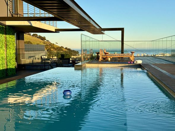 Infinity pool overlooking a marina at sunset, with mountains and a bridge in the distance