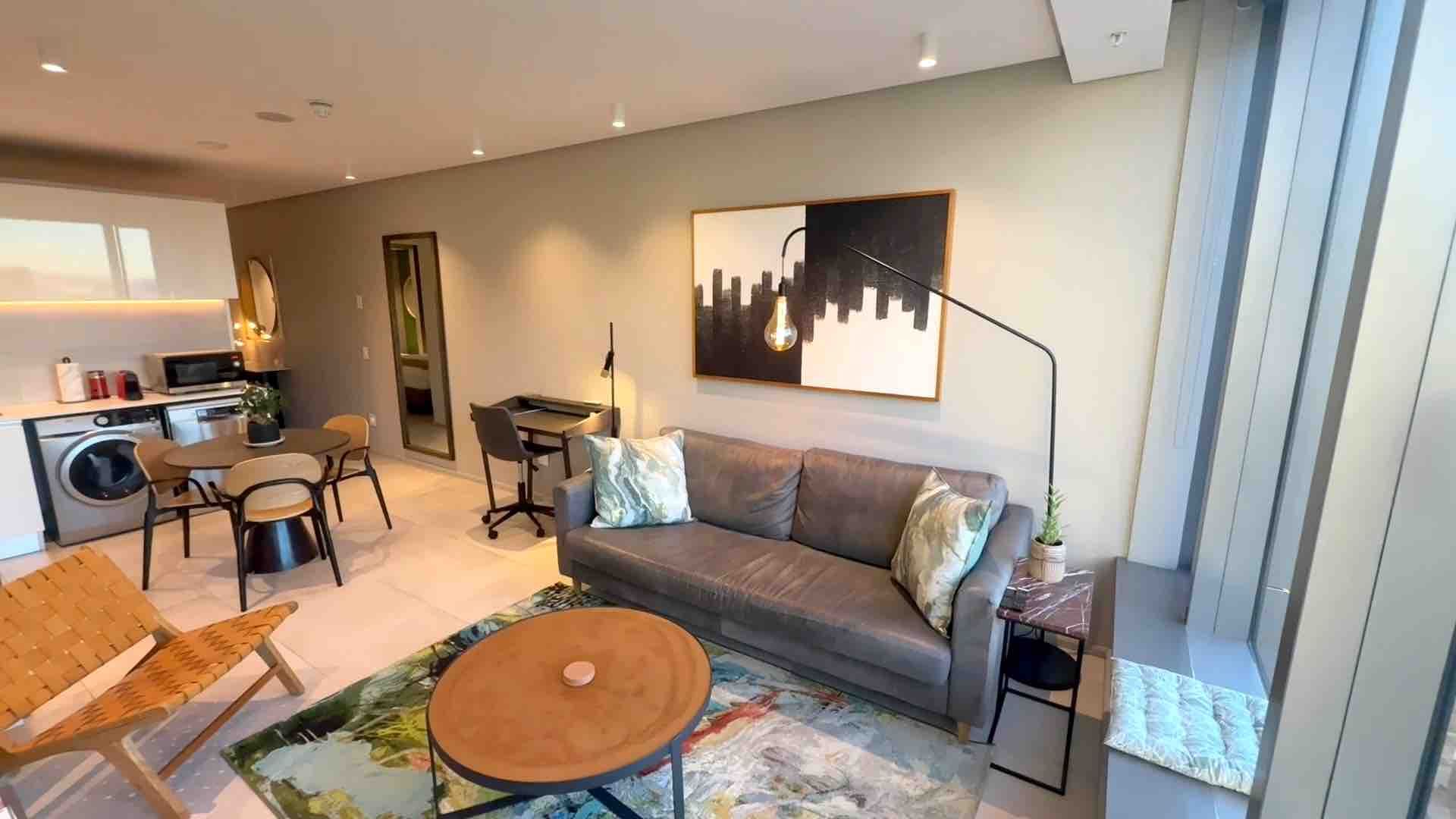 Modern open-plan living room with gray sofa, round coffee table, rug, and dining area