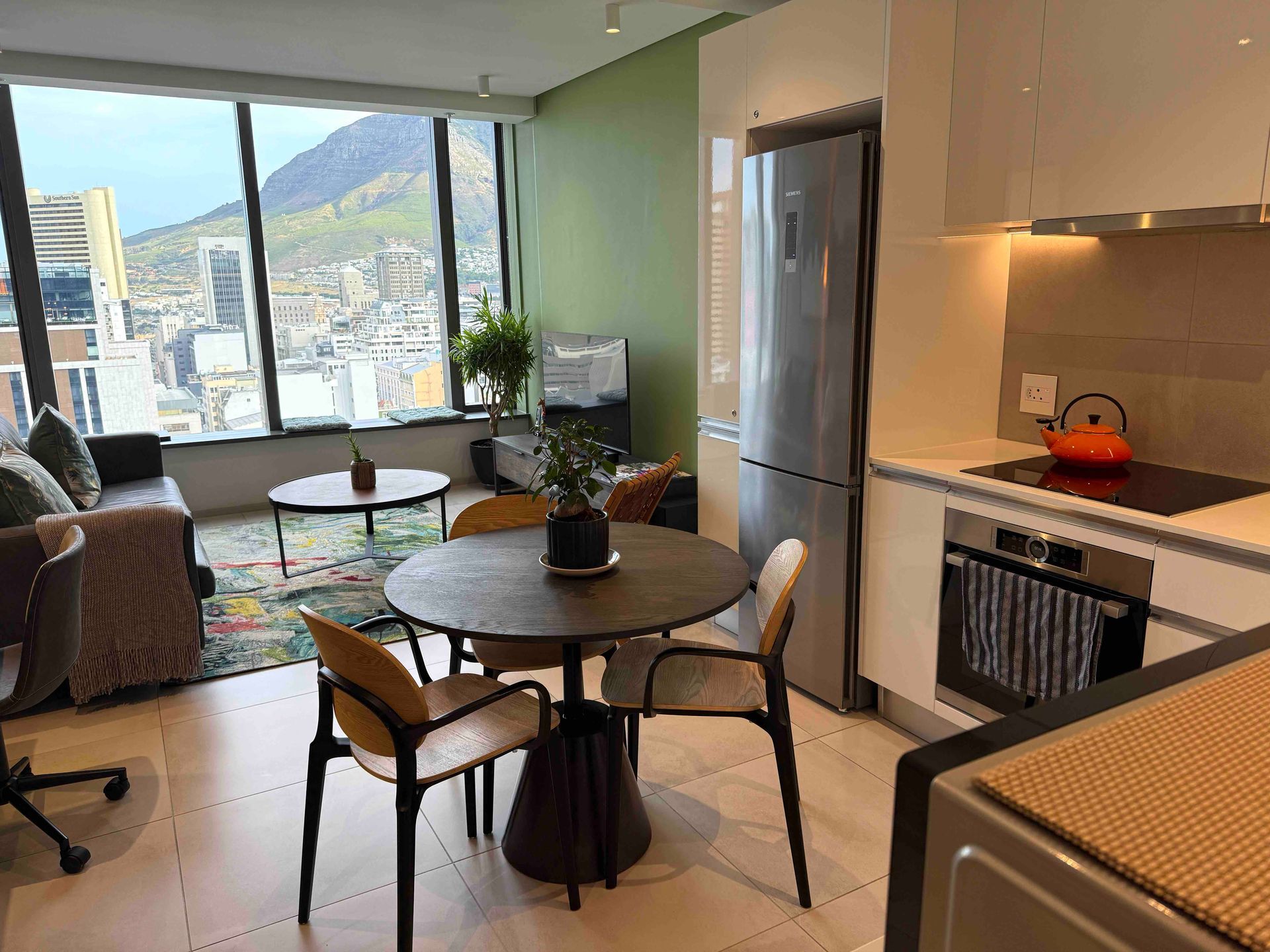 Modern apartment living room and kitchen with round table, couch, and city view through large windows
