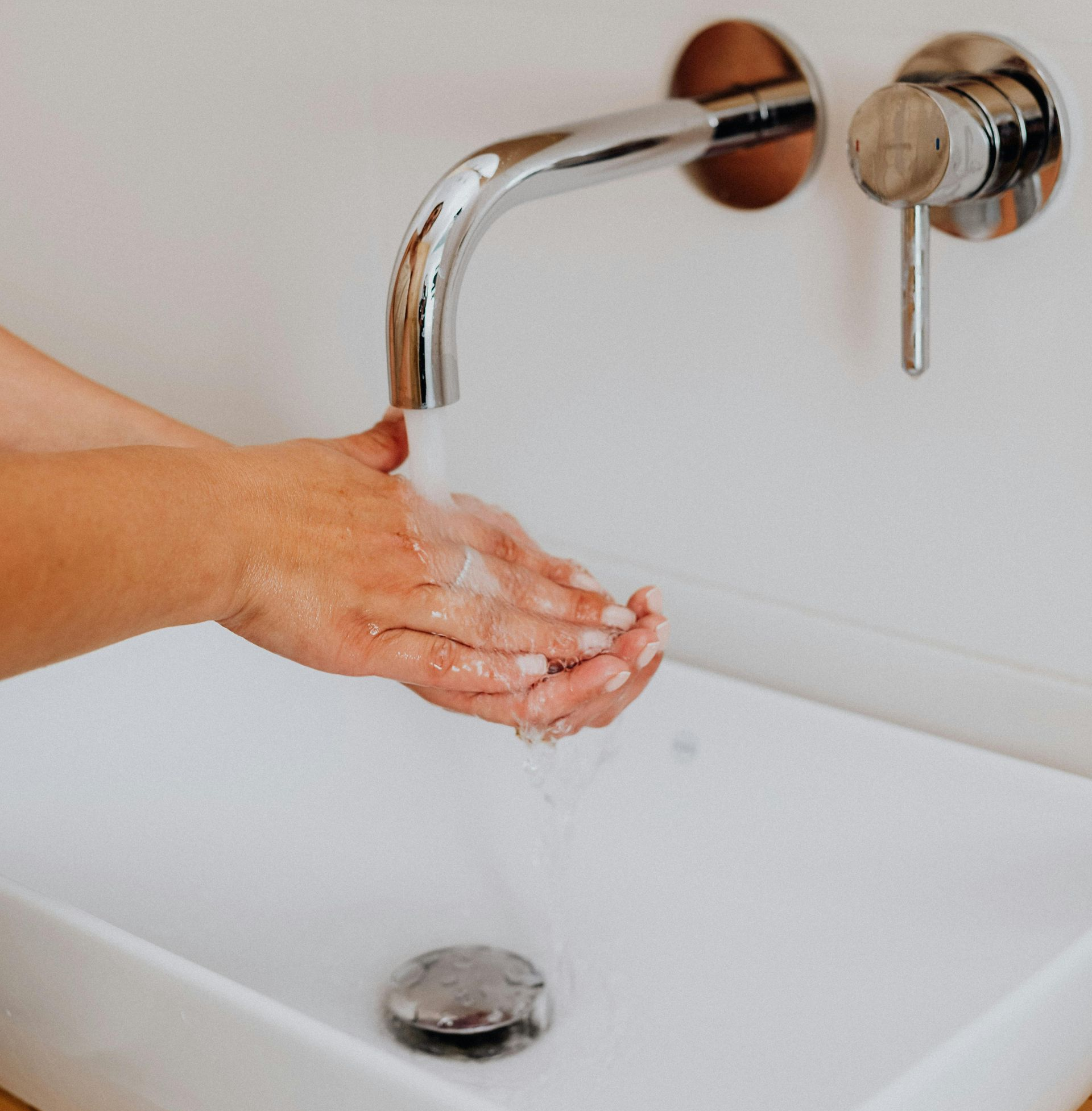 Person washing hands under a chrome faucet in a white sink.