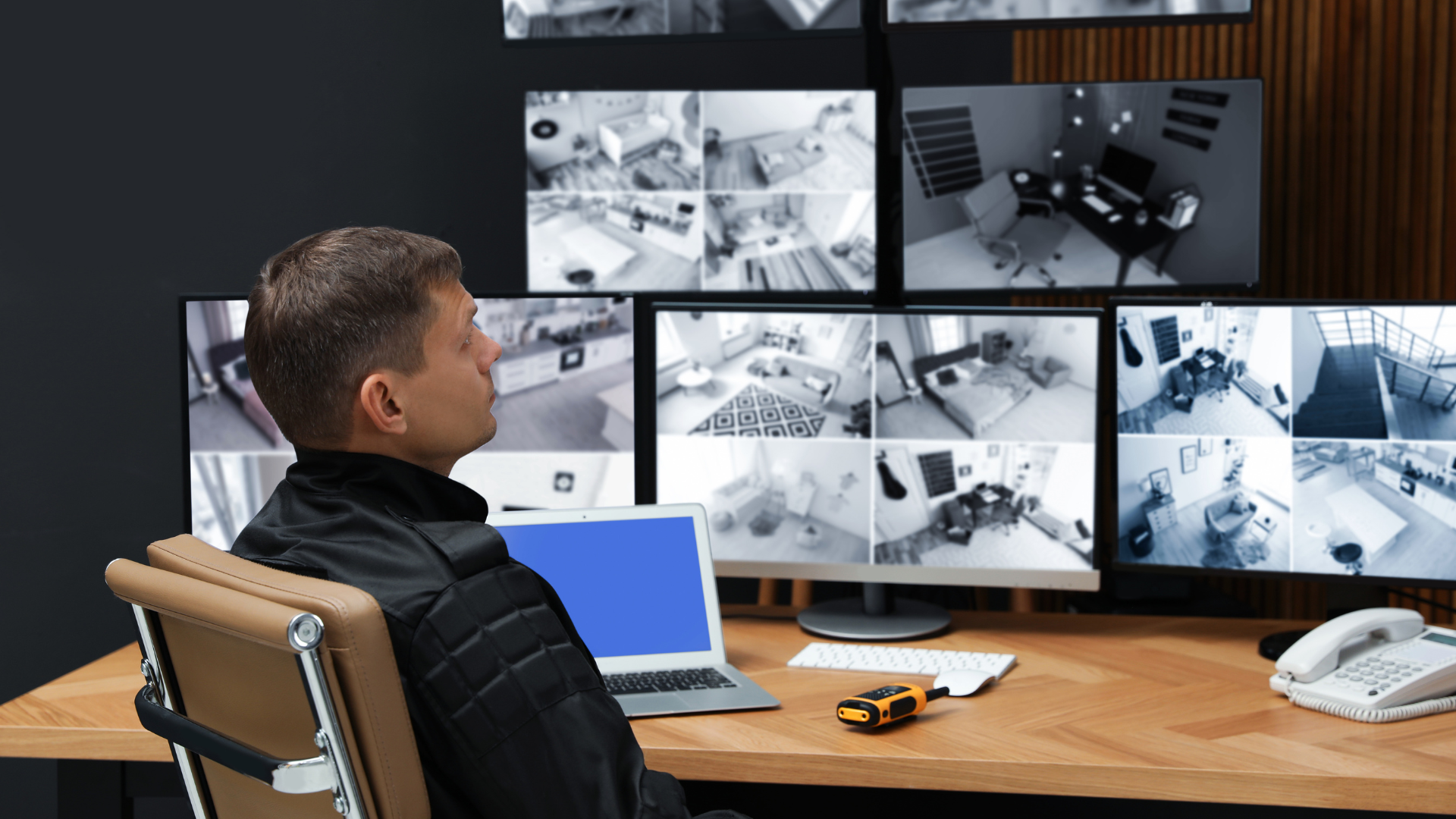A man wearing headphones is talking on a cell phone while sitting in front of a computer.
