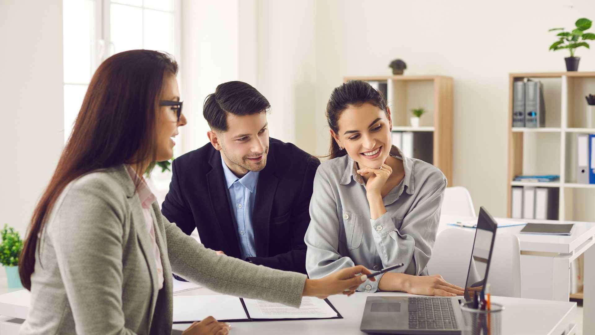 A man and a woman are sitting at a table looking at a laptop.