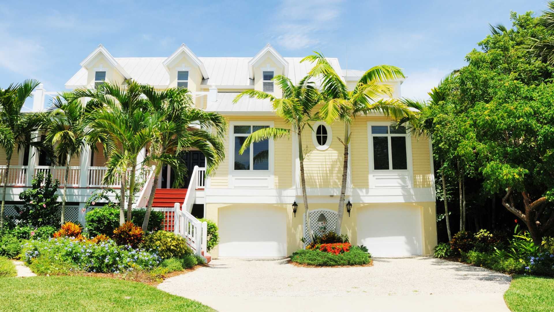 A large yellow house with white trim and palm trees in front of it