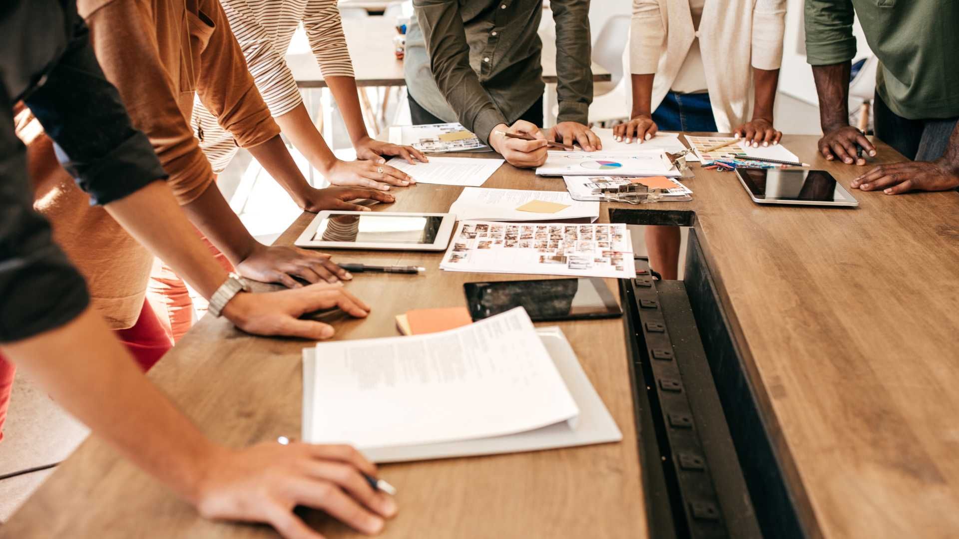A group of people are standing around a wooden table.