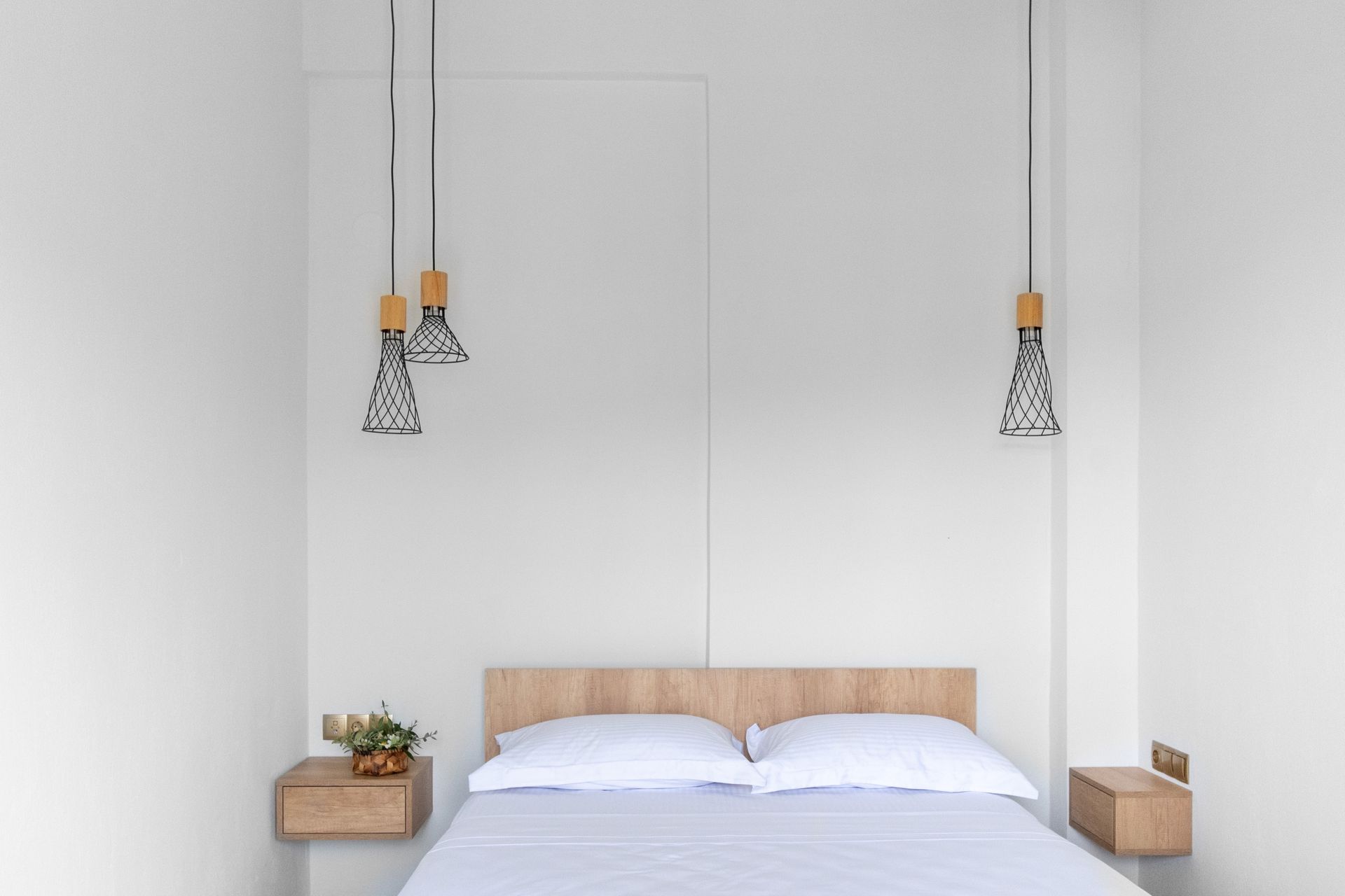 A bedroom with a bed , nightstands , and lamps hanging from the ceiling.