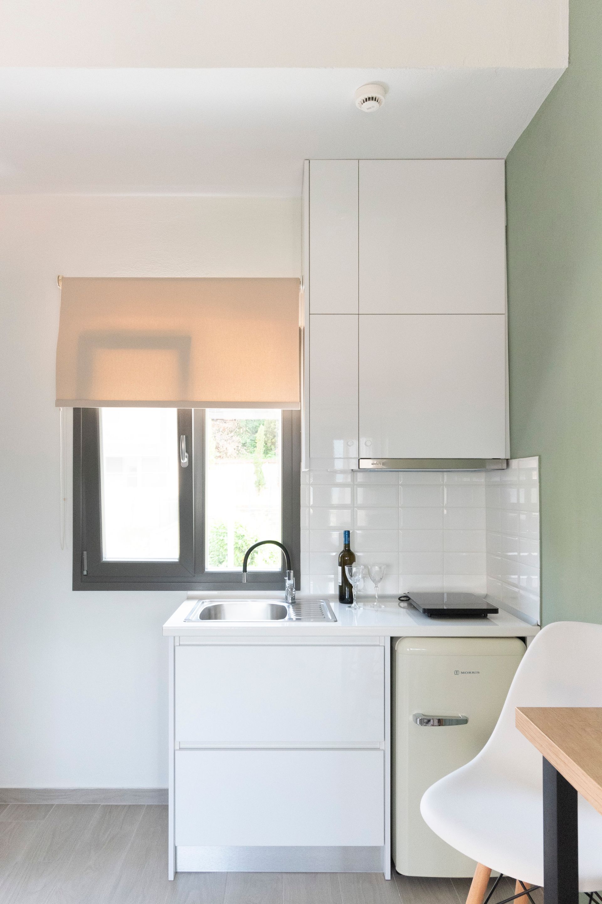 A kitchen with white cabinets , a sink , a refrigerator and a window.