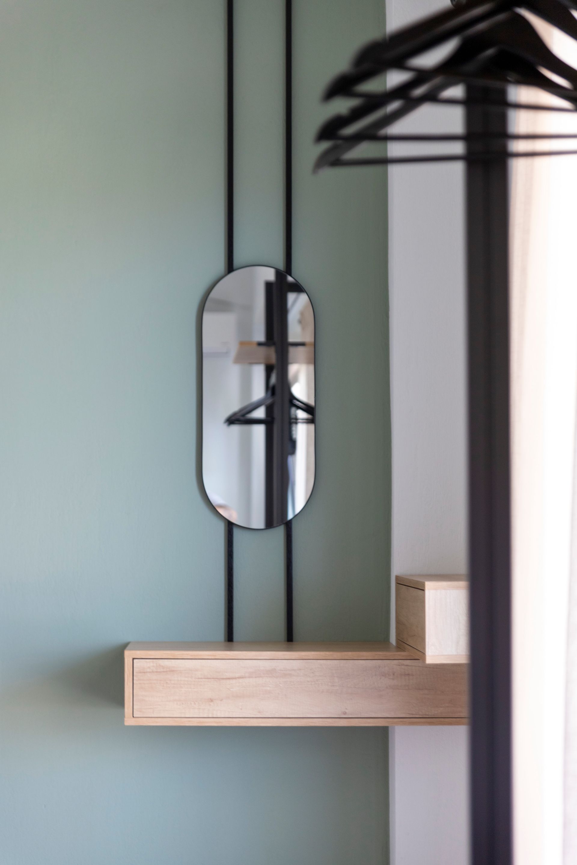 A mirror is hanging on a wall next to a shelf with clothes hanging on it.