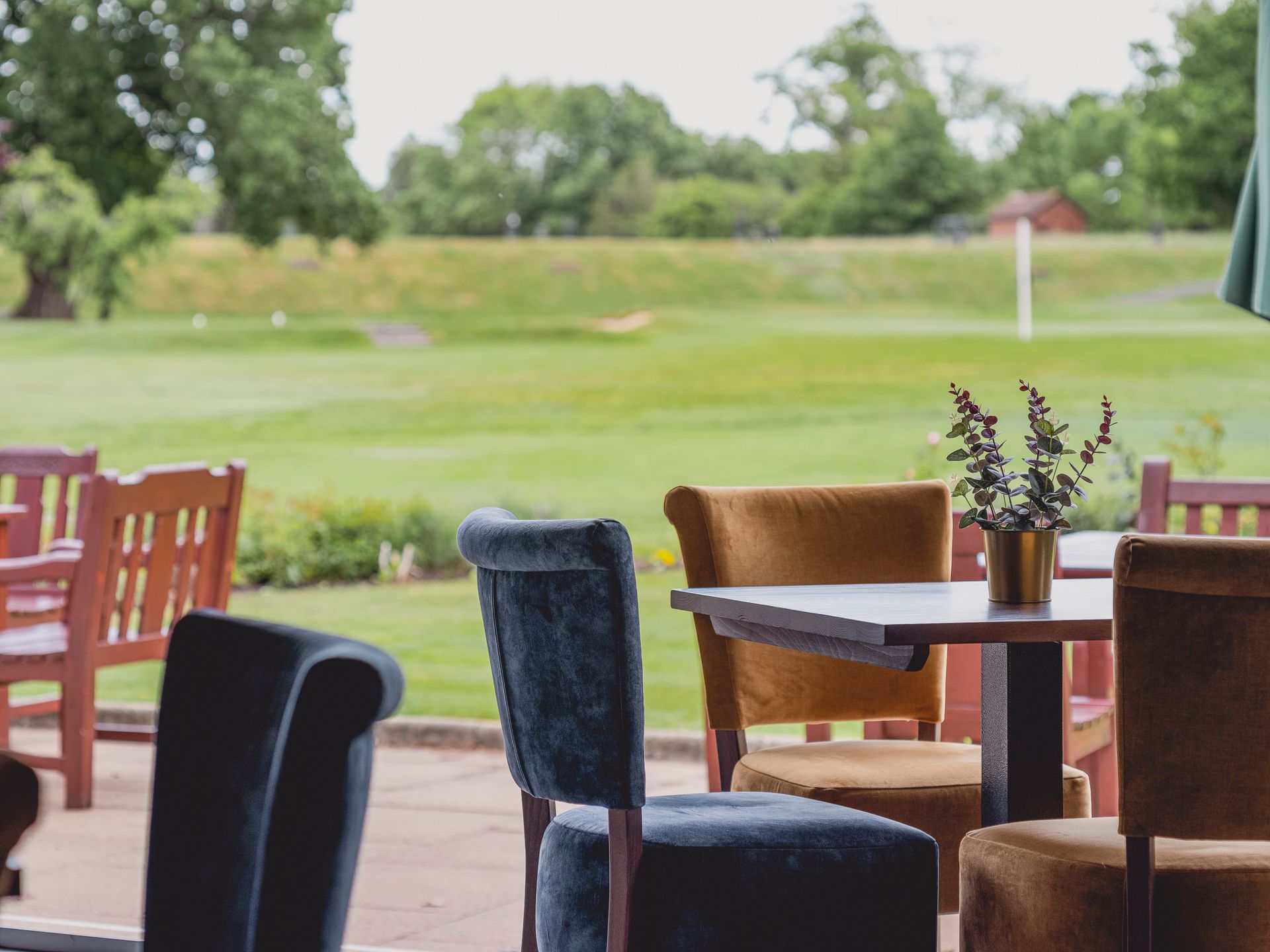 Clubhouse terrace seating with blue and mustard chairs overlooking the golf course and putting green.
