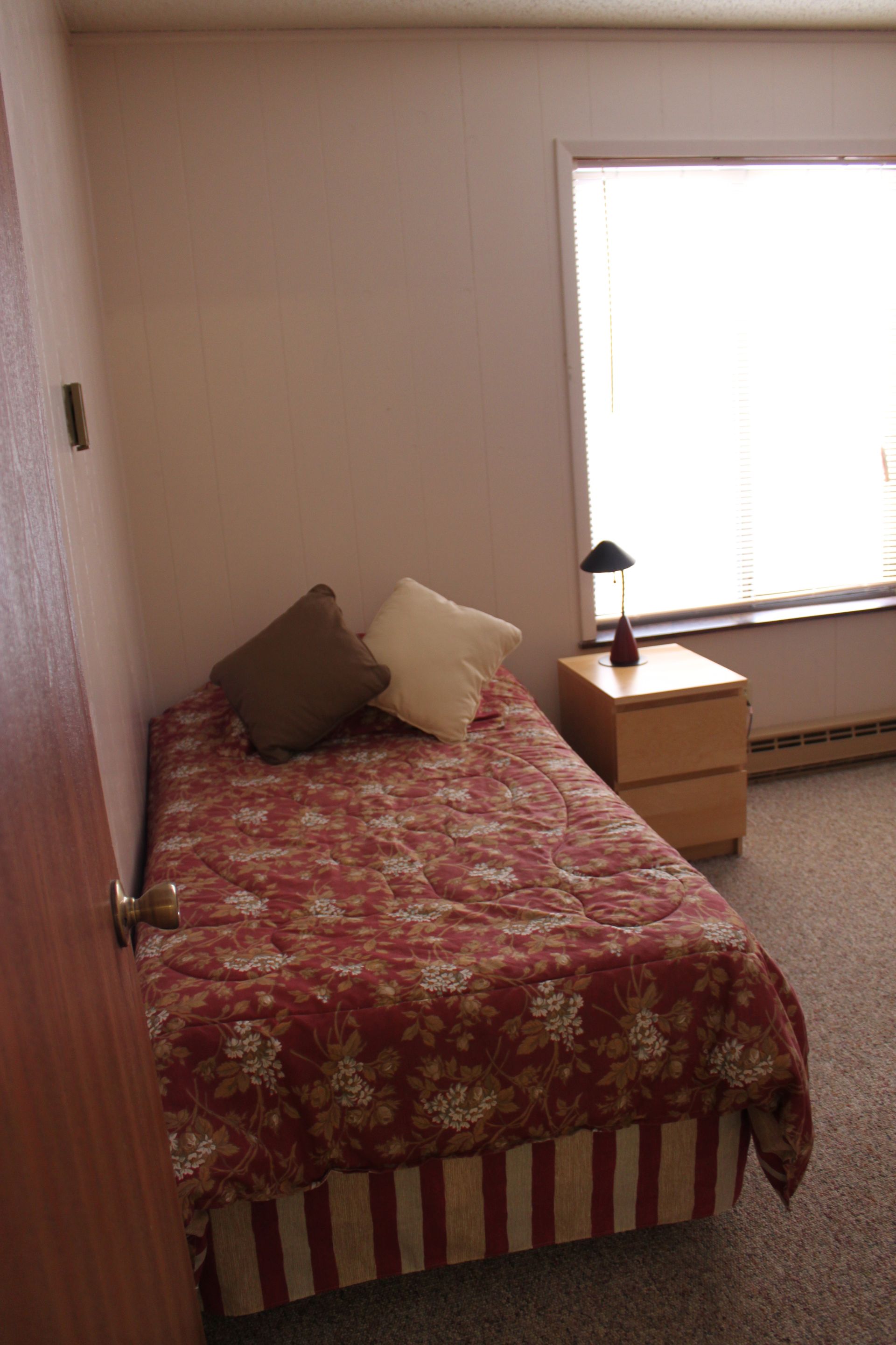 Photo showing a twin-size bed in a bedroom with a window in the background