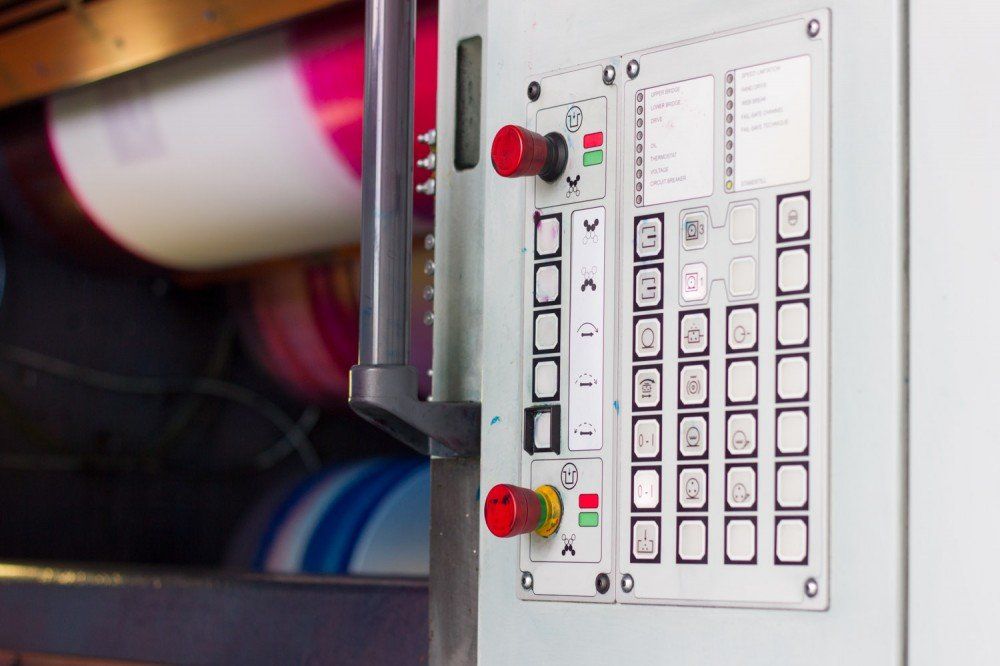 Control panel of a printing press with buttons and a rotating cylinder in the background.