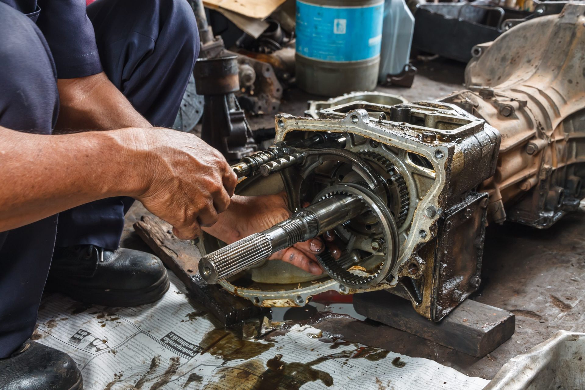 Mechanic repairing a gearbox on a workbench, with greasy tools and metal parts visible.