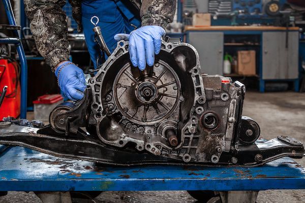 Mechanic in blue gloves working on a disassembled car transmission on a workshop bench