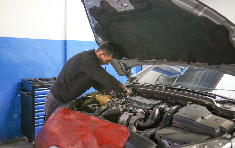 Mechanic inspecting a car engine with the hood open in a garage