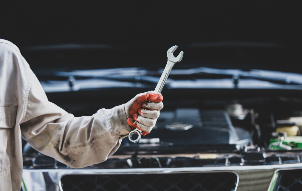 Mechanic holding a wrench in front of an open car hood in a garage