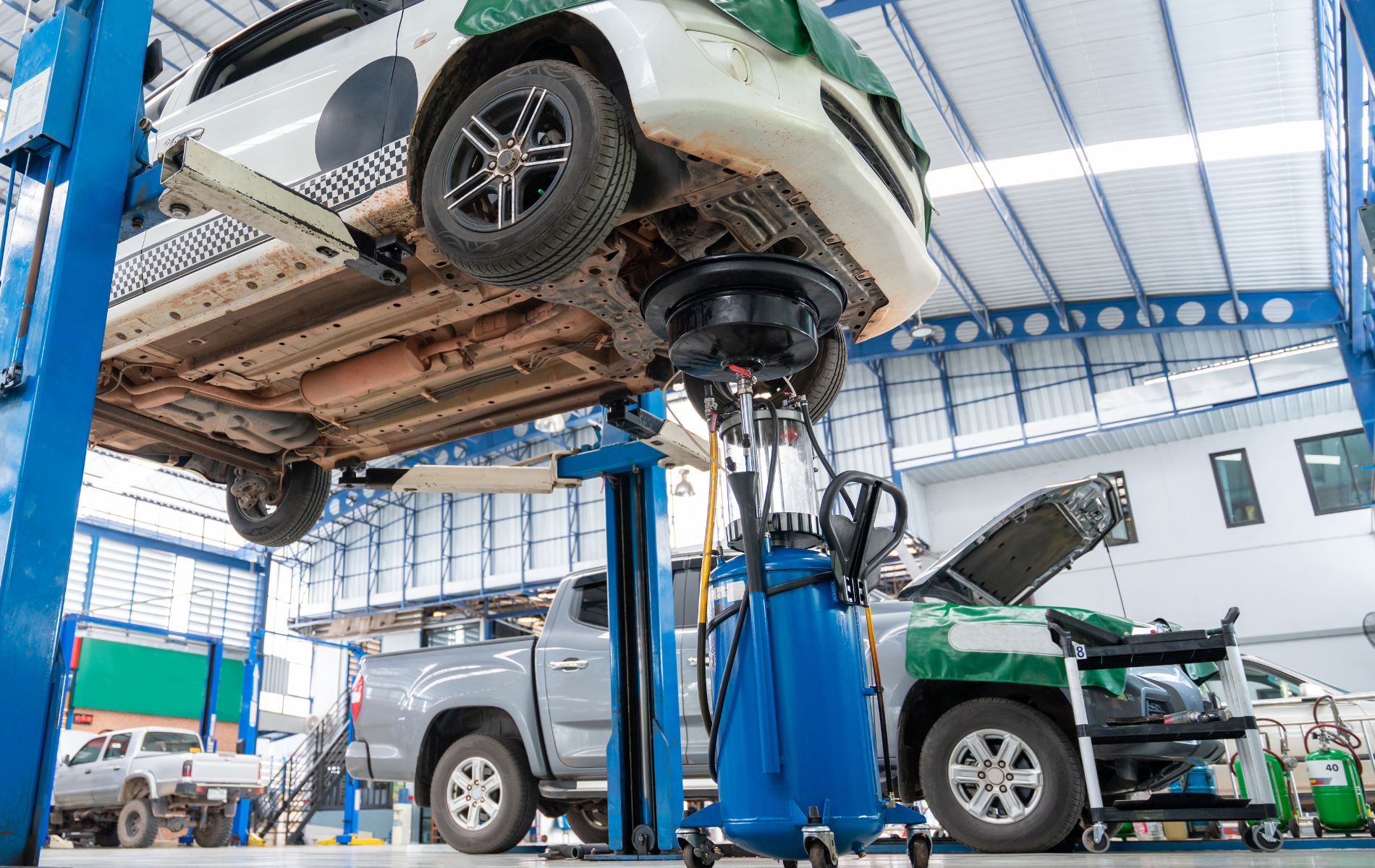 Car lifted on a blue hydraulic hoist in an auto repair shop with another vehicle nearby