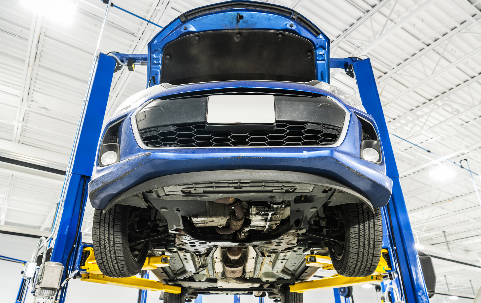 Blue car lifted on a service bay in an auto repair shop, underside visible on a hydraulic lift
