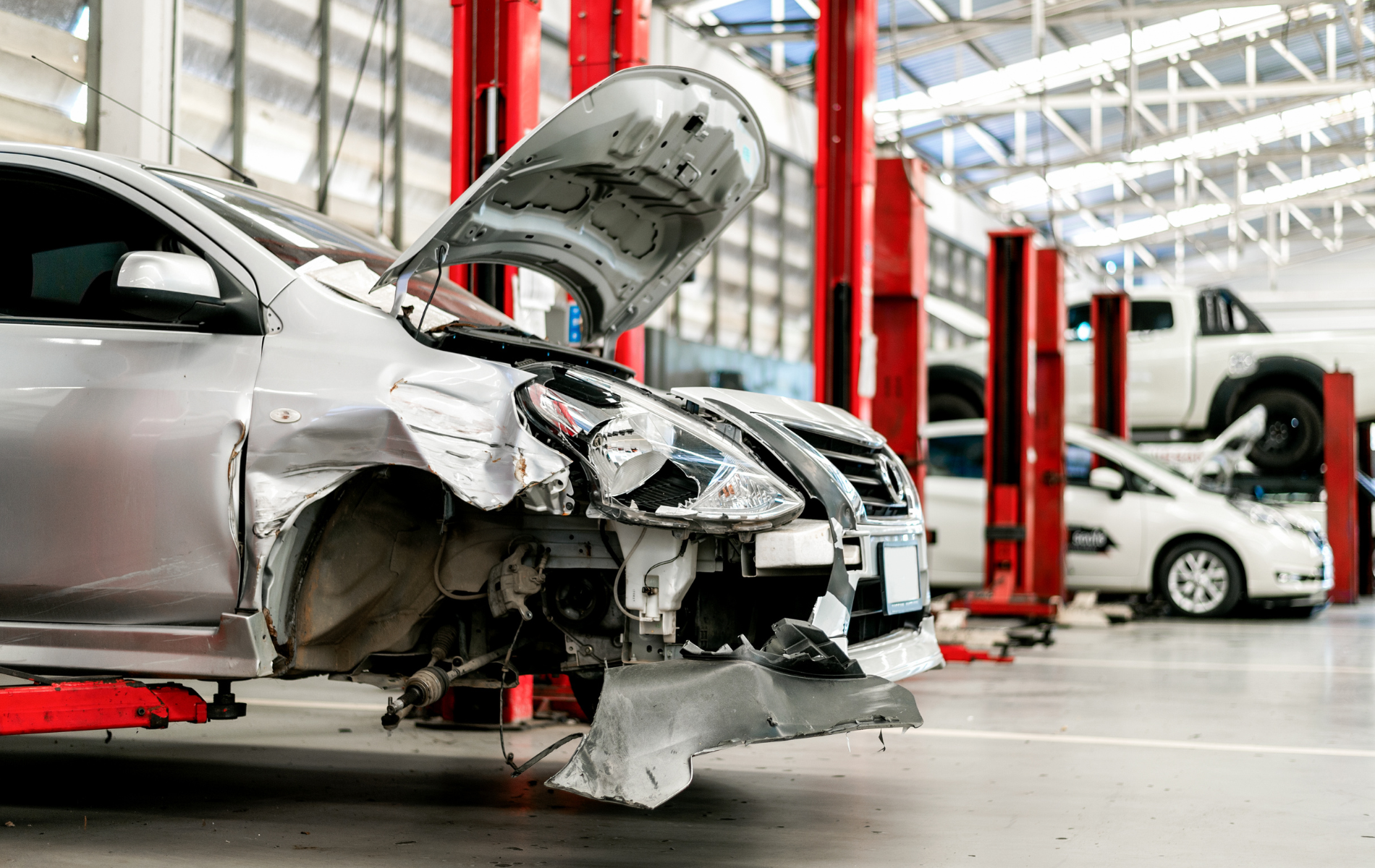 Damaged silver car in auto repair shop with hood open and front-end collision damage