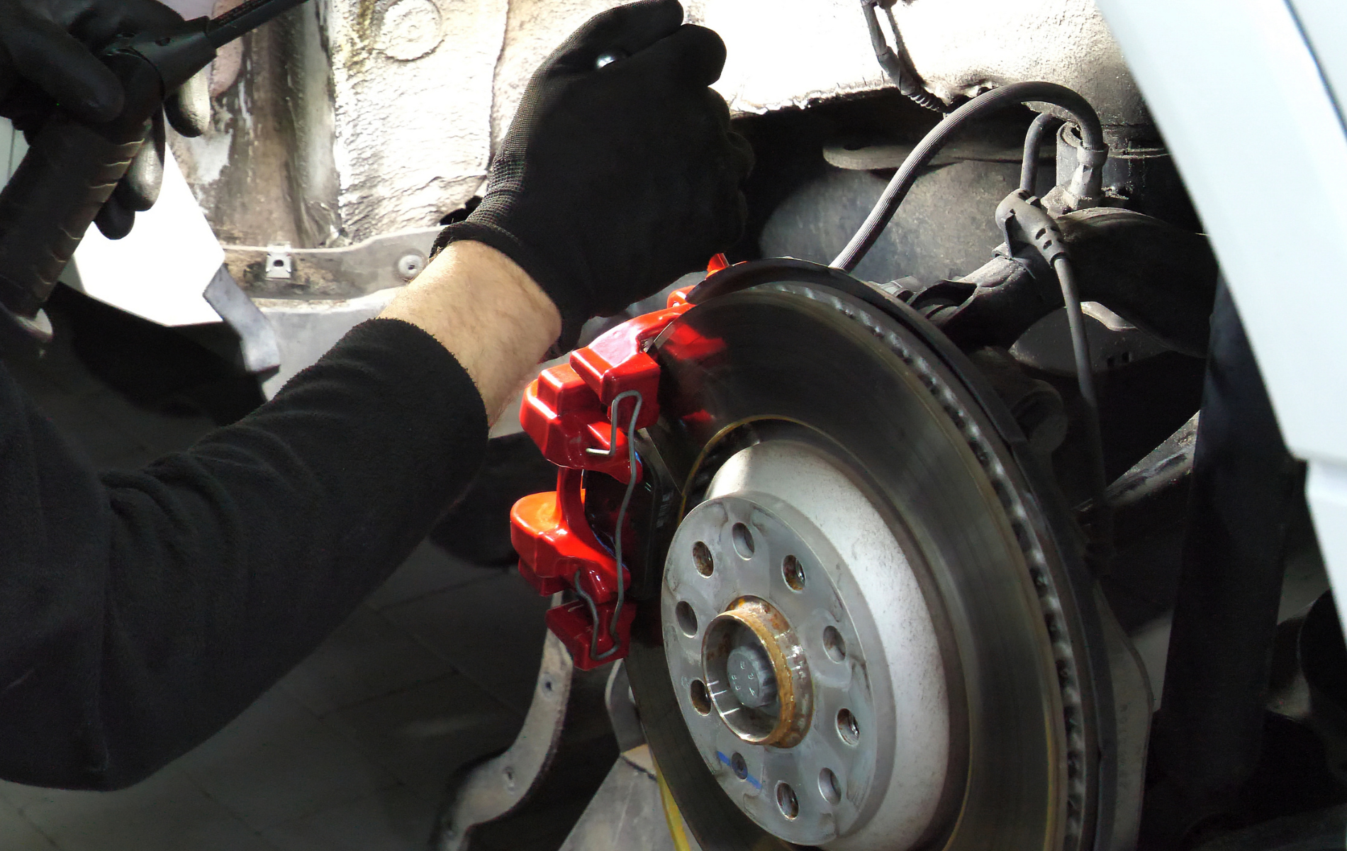 Mechanic working on a car’s red brake caliper and rotor inside the wheel well