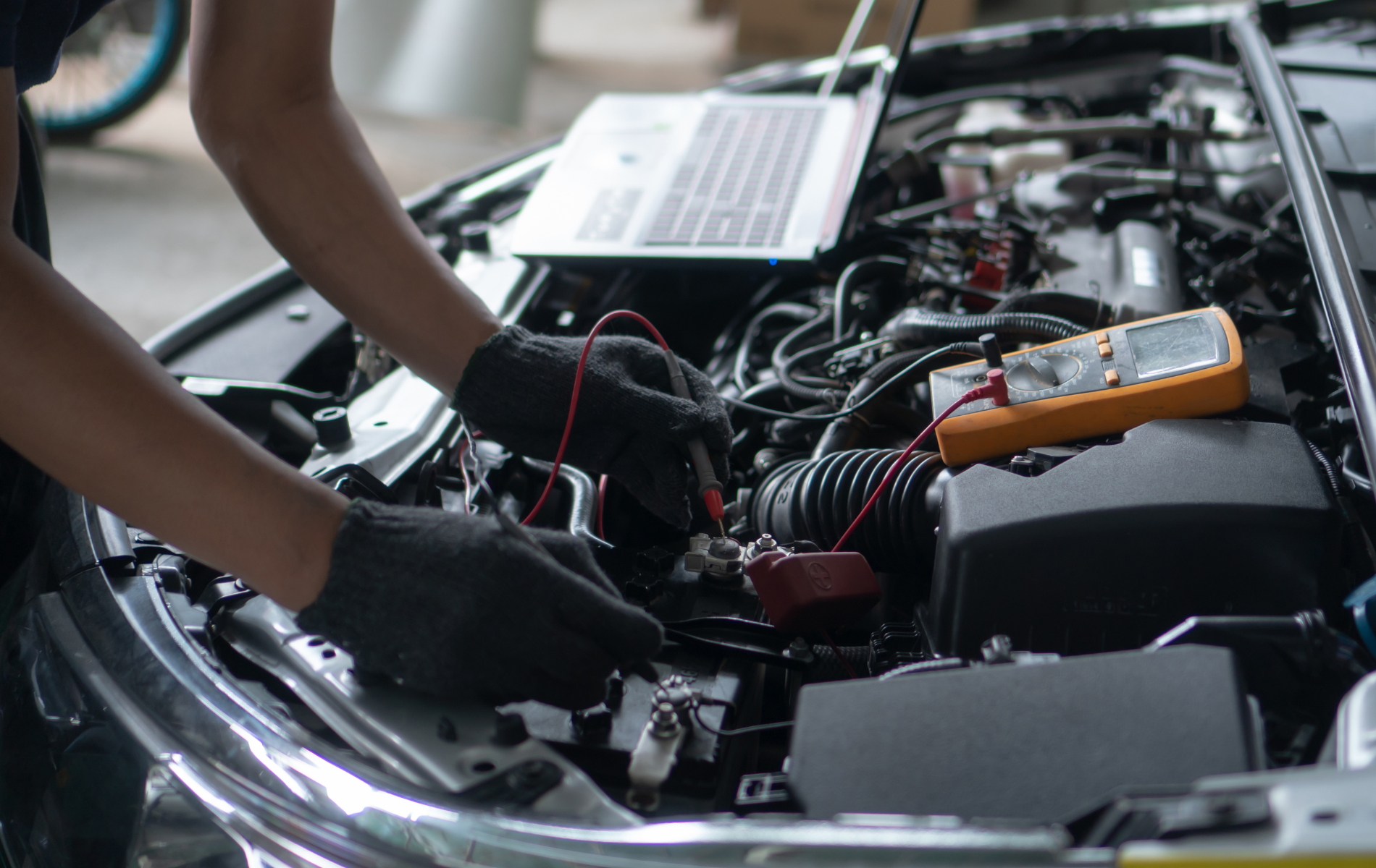 Mechanic using a multimeter to test wiring in an open car engine bay
