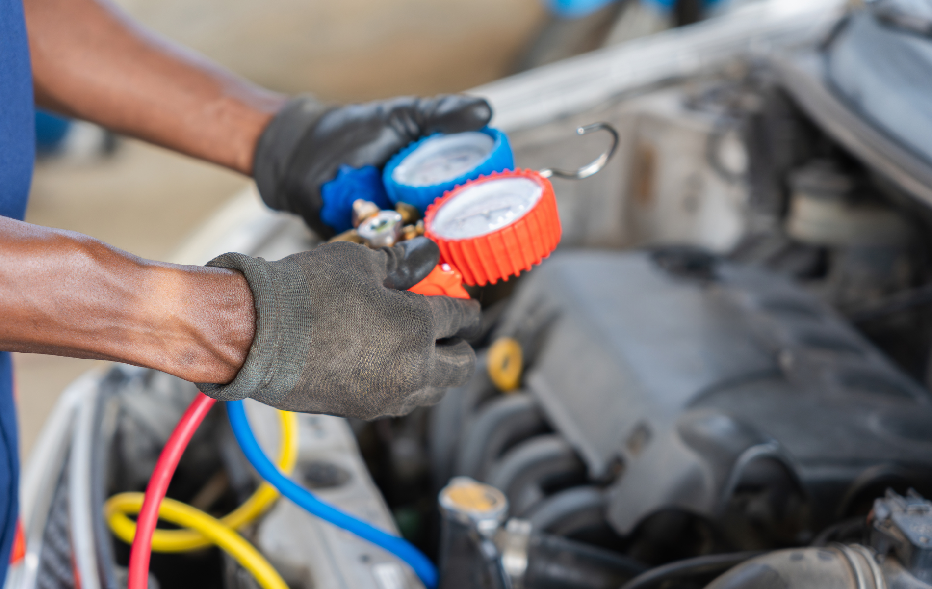 Mechanic using gauges to service a car engine with hoses attached