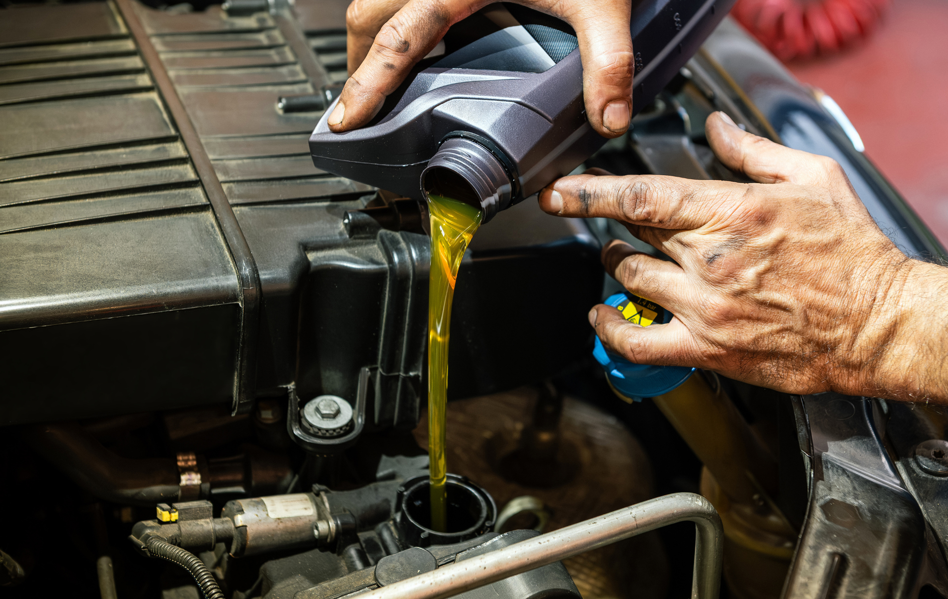 Hands pouring yellow motor oil into a car engine compartment